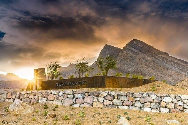 The Reverence community entrance sign at sunset, set into a desert stone wall with the Red Rock mountains rising behind it