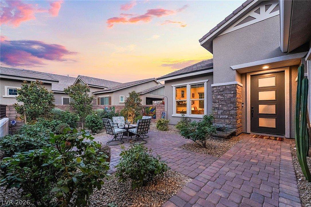 The private courtyard at dusk: a paver patio with seating under mature trees, planters, and the modern glass-panel front door framed by stone