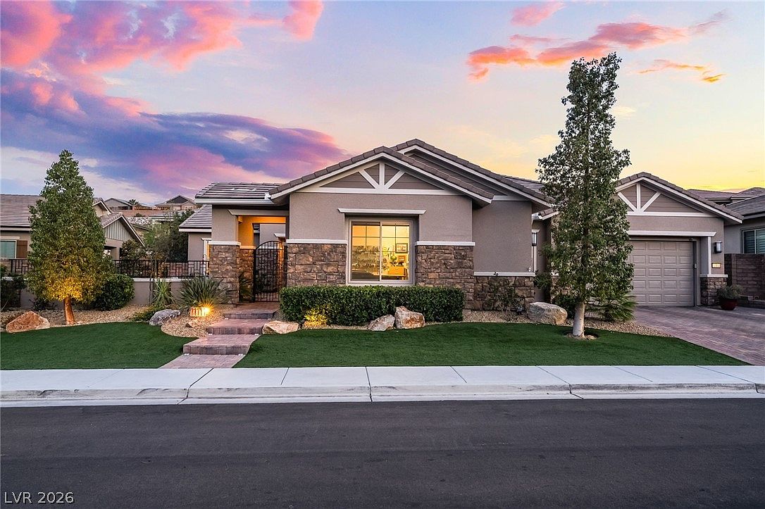 Twilight front elevation of 11111 Luna Blanca Drive, a single-story stone-and-stucco home with stacked-stone columns, lit interiors, and a pastel sunset sky in the Reverence community of Summerlin, Las Vegas